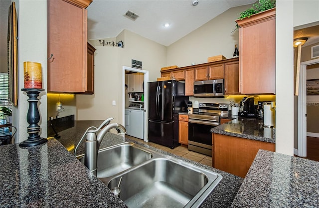 kitchen with sink, high vaulted ceiling, dark stone countertops, stainless steel appliances, and washer and clothes dryer