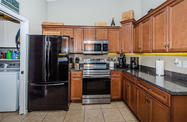 kitchen with light tile patterned flooring, stainless steel appliances, washer and dryer, and dark stone counters