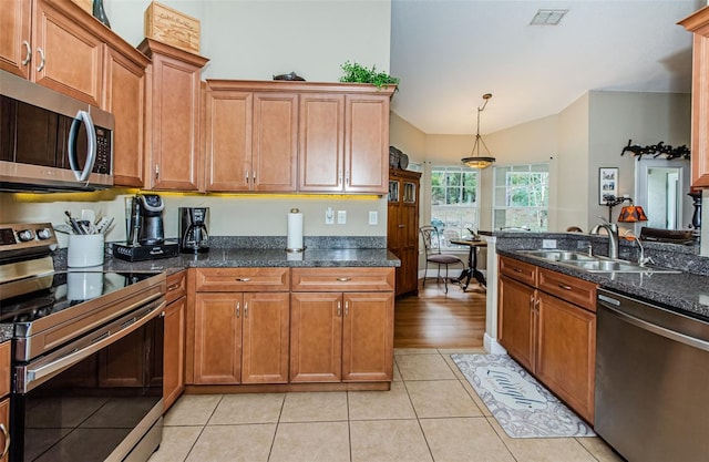 kitchen with pendant lighting, sink, stainless steel appliances, light tile patterned flooring, and dark stone counters