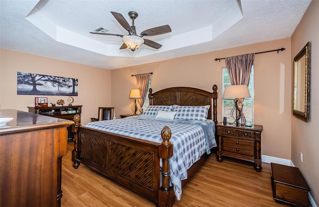 bedroom featuring a tray ceiling, light hardwood / wood-style flooring, and a textured ceiling