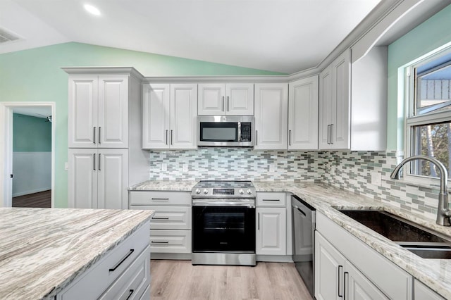 kitchen featuring lofted ceiling, sink, light stone counters, and appliances with stainless steel finishes