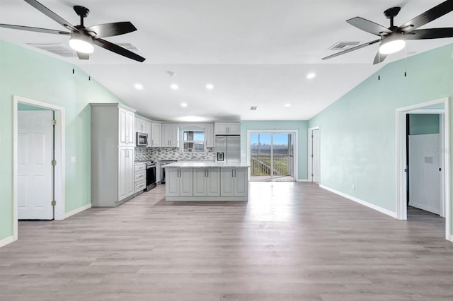 kitchen featuring lofted ceiling, appliances with stainless steel finishes, a center island, tasteful backsplash, and light wood-type flooring