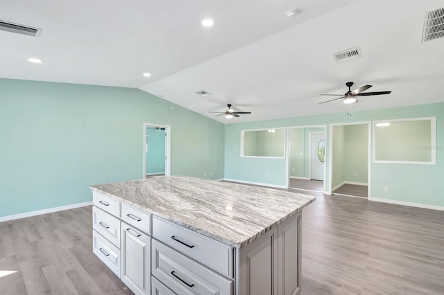 kitchen featuring a center island, vaulted ceiling, light wood-type flooring, light stone countertops, and white cabinets