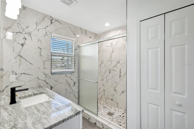 bathroom with vanity, a shower with shower door, and tile walls