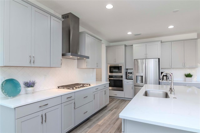 kitchen with wall chimney exhaust hood, sink, gray cabinets, stainless steel appliances, and light hardwood / wood-style floors