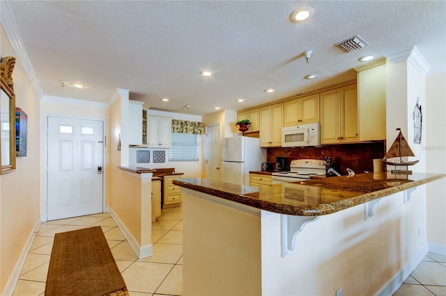 kitchen with light tile patterned floors, white appliances, a kitchen breakfast bar, and kitchen peninsula