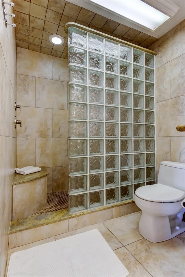 bathroom with tile patterned flooring, tiled shower, tile walls, and toilet