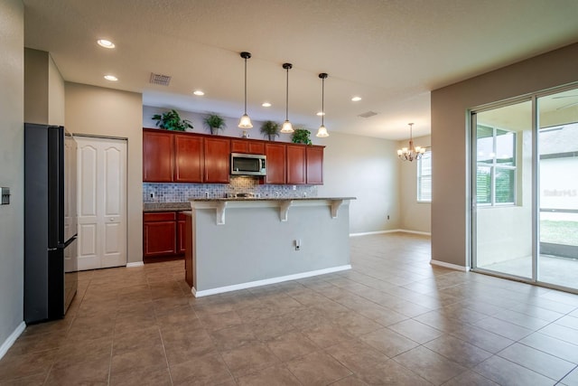 kitchen with a breakfast bar area, tasteful backsplash, black refrigerator, pendant lighting, and a kitchen island with sink