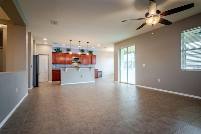 kitchen with a kitchen island with sink, hanging light fixtures, a kitchen bar, light tile patterned flooring, and decorative backsplash