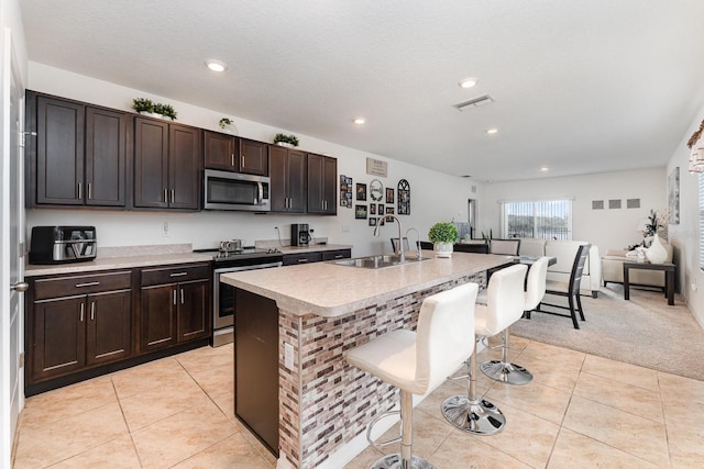 kitchen featuring a kitchen island with sink, sink, light tile patterned floors, and stainless steel appliances