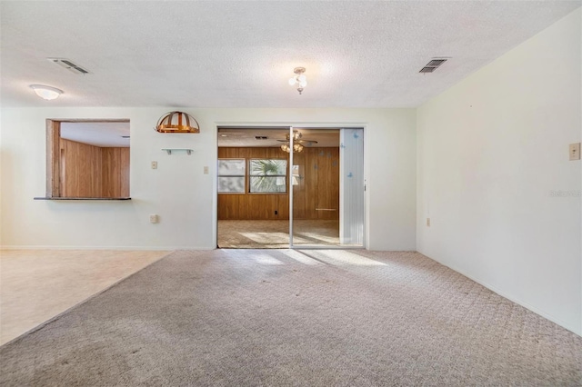 carpeted empty room featuring ceiling fan, a textured ceiling, and wood walls