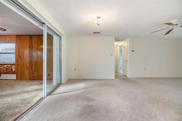 carpeted empty room with ceiling fan, wooden walls, and a textured ceiling