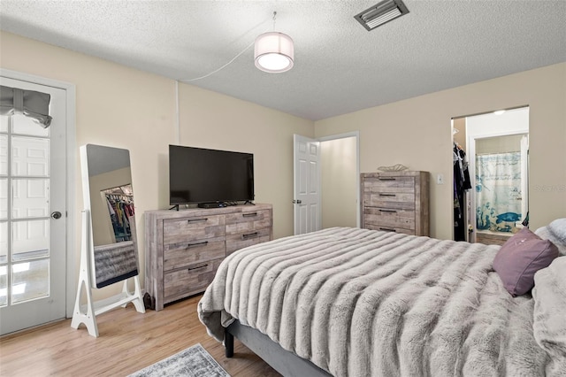 bedroom with a spacious closet, a textured ceiling, a closet, and light hardwood / wood-style flooring