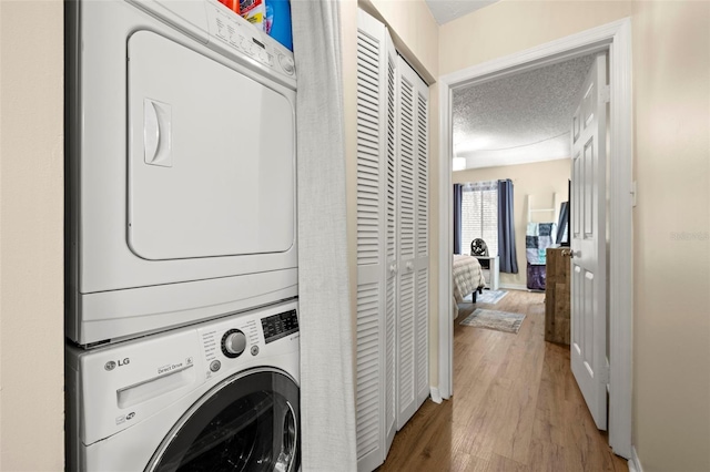 laundry room with hardwood / wood-style flooring, stacked washer and dryer, and a textured ceiling