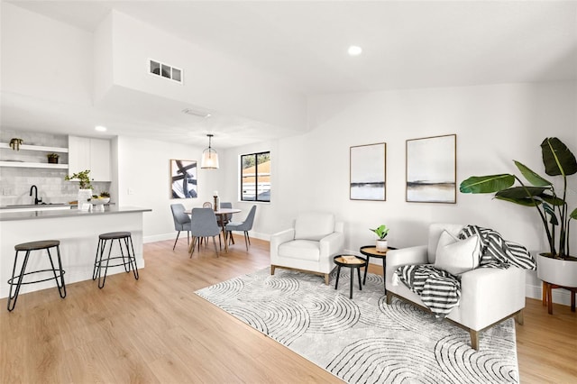 living area featuring lofted ceiling, sink, and light wood-type flooring