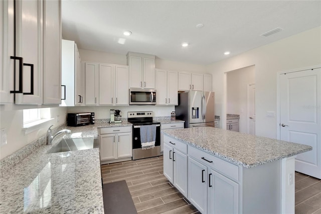 kitchen with appliances with stainless steel finishes, white cabinetry, sink, a center island, and light stone counters