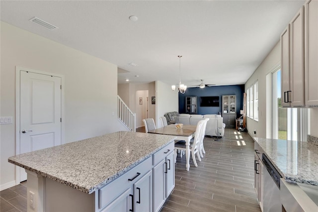 kitchen with a kitchen island, pendant lighting, dishwasher, white cabinets, and light stone counters