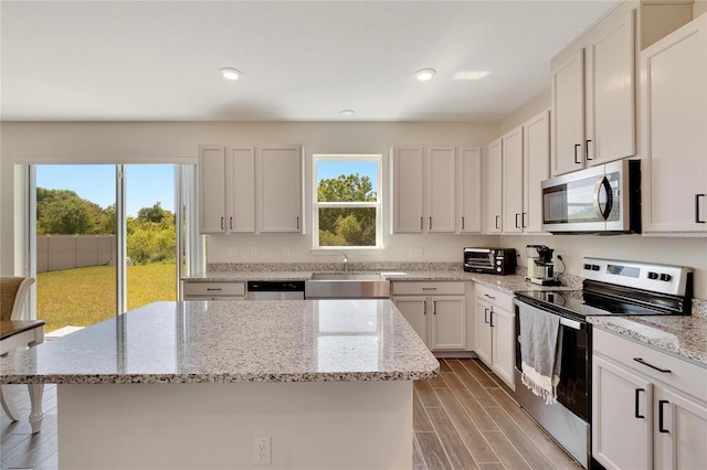 kitchen with white cabinetry, appliances with stainless steel finishes, light stone countertops, and a kitchen island