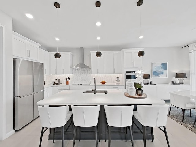 kitchen with wall chimney range hood, sink, white cabinetry, hanging light fixtures, and stainless steel appliances