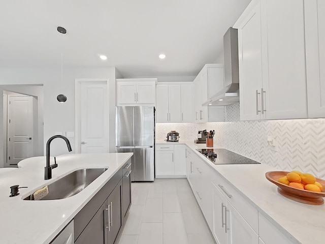 kitchen with white cabinetry, wall chimney range hood, decorative light fixtures, and stainless steel refrigerator