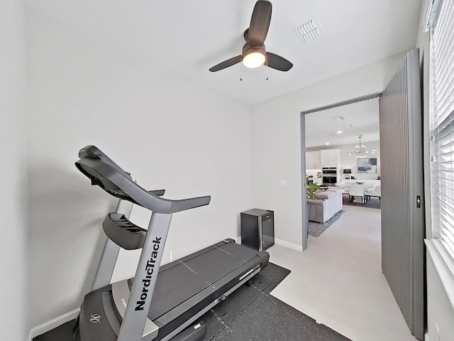 workout area featuring ceiling fan with notable chandelier