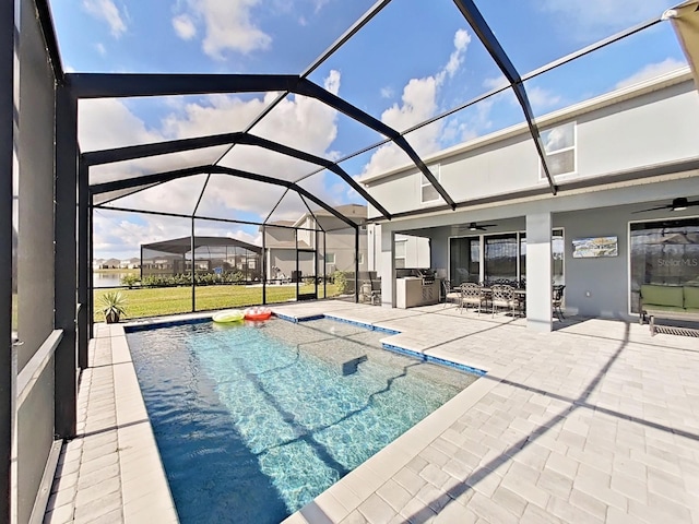 view of swimming pool with a patio, an outdoor kitchen, ceiling fan, and glass enclosure