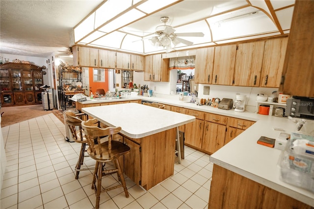 kitchen featuring a kitchen island, a breakfast bar, light tile patterned floors, ceiling fan, and kitchen peninsula