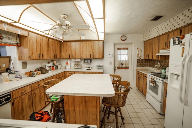 kitchen with a breakfast bar, a textured ceiling, light tile patterned floors, a kitchen island, and white appliances