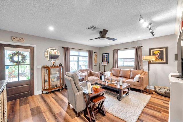 living room featuring ceiling fan, wood-type flooring, a textured ceiling, and a wealth of natural light