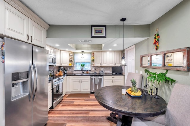 kitchen with sink, hanging light fixtures, stainless steel appliances, light hardwood / wood-style floors, and backsplash