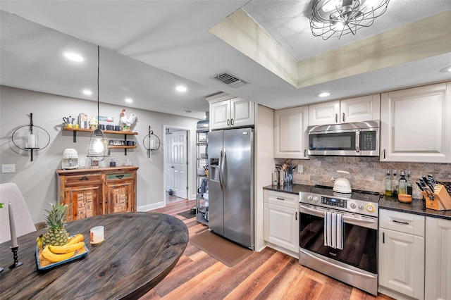 kitchen with stainless steel appliances, white cabinetry, backsplash, and light hardwood / wood-style flooring