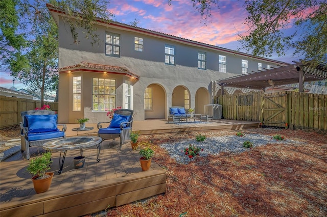 back house at dusk with a pergola, outdoor lounge area, and a wooden deck