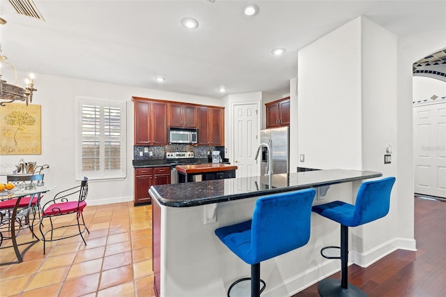 kitchen featuring appliances with stainless steel finishes, hanging light fixtures, decorative backsplash, light tile patterned flooring, and a breakfast bar