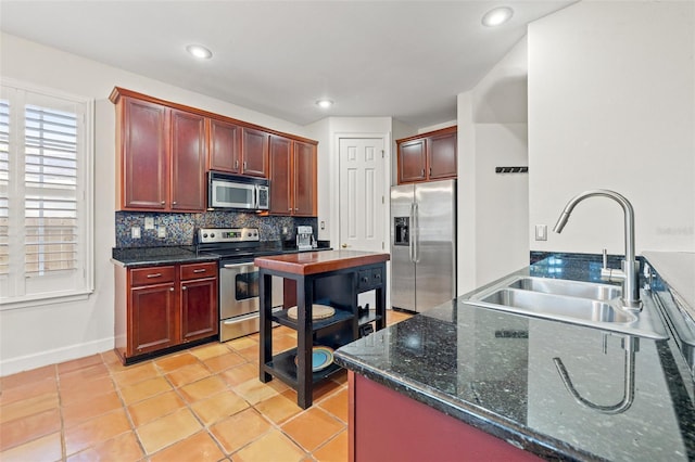 kitchen with appliances with stainless steel finishes, dark stone counters, backsplash, light tile patterned floors, and sink