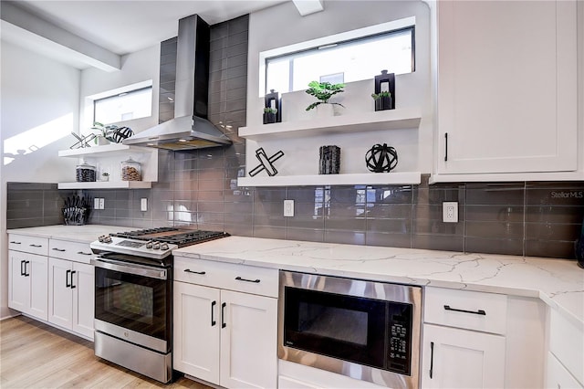 kitchen featuring built in microwave, wall chimney range hood, stainless steel range with gas cooktop, and light stone countertops