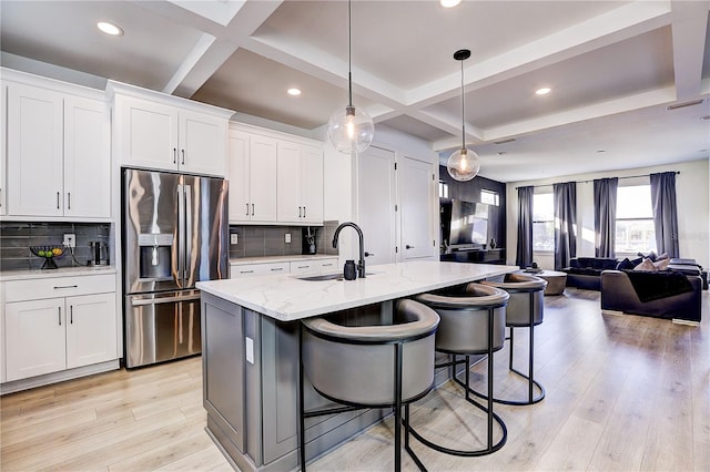 kitchen with stainless steel refrigerator with ice dispenser, an island with sink, hanging light fixtures, and white cabinets