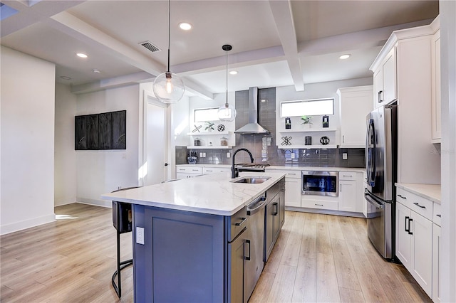 kitchen featuring stainless steel appliances, an island with sink, wall chimney range hood, and white cabinets