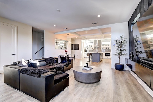 living room with coffered ceiling, beam ceiling, sink, and light hardwood / wood-style flooring