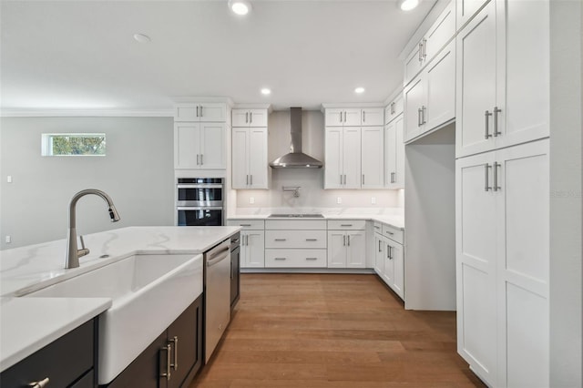 kitchen featuring white cabinets, light stone countertops, sink, and wall chimney range hood