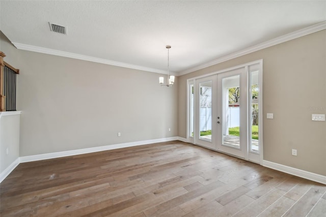 spare room featuring crown molding, an inviting chandelier, light hardwood / wood-style floors, and french doors