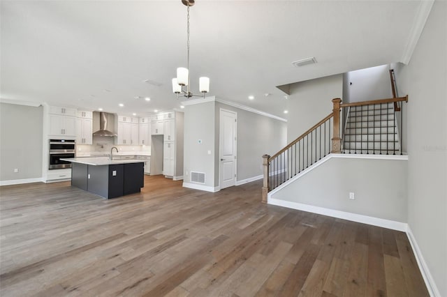 kitchen featuring pendant lighting, sink, a kitchen island with sink, white cabinetry, and wall chimney exhaust hood