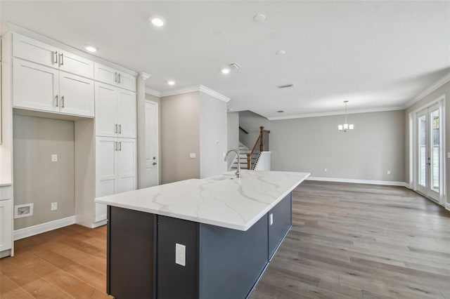 kitchen with pendant lighting, white cabinets, a kitchen island with sink, light stone countertops, and light hardwood / wood-style flooring