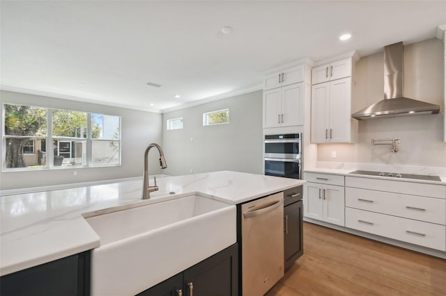 kitchen featuring sink, appliances with stainless steel finishes, wall chimney range hood, light stone countertops, and white cabinets