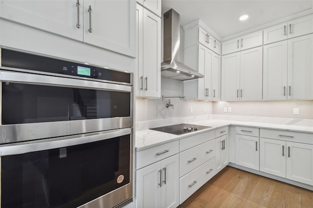 kitchen with double oven, wall chimney range hood, white cabinets, and black electric stovetop