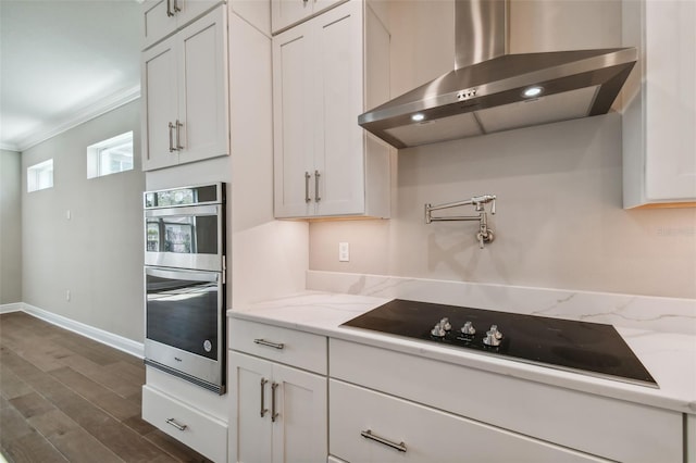 kitchen with white cabinetry, wall chimney range hood, light stone countertops, and black electric stovetop