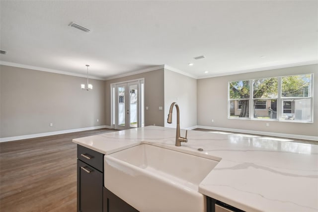 kitchen featuring sink, hanging light fixtures, ornamental molding, light stone counters, and dark wood-type flooring