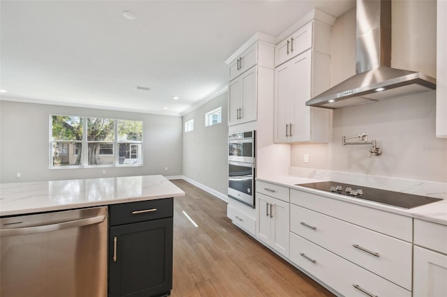 kitchen featuring stainless steel appliances, wall chimney range hood, and white cabinets