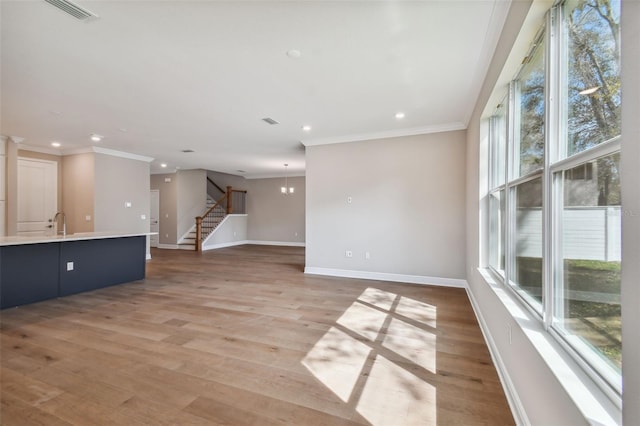 unfurnished living room featuring crown molding, sink, and light hardwood / wood-style floors