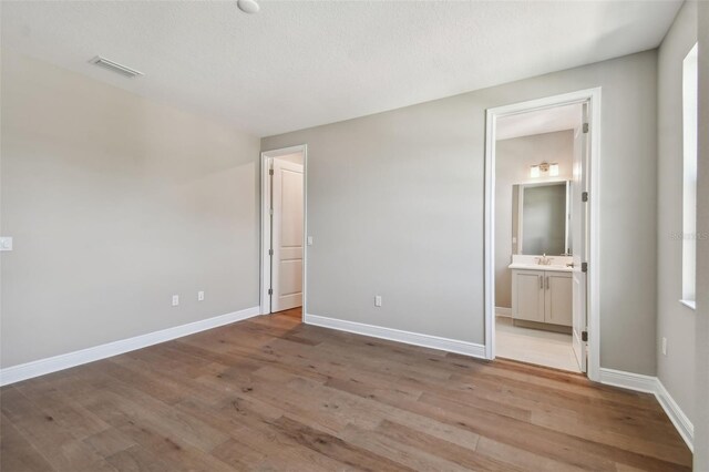 unfurnished bedroom with ensuite bathroom and light hardwood / wood-style floors