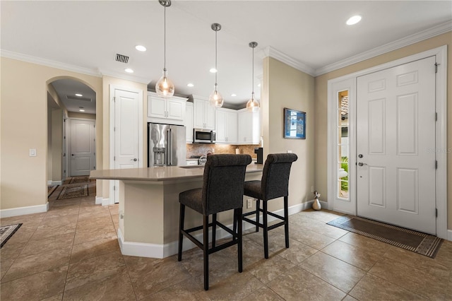 kitchen with crown molding, a breakfast bar area, stainless steel appliances, white cabinets, and decorative light fixtures